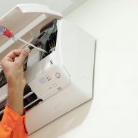 Hands of technician using screwdriver when installing air conditioner in bedroom of customer